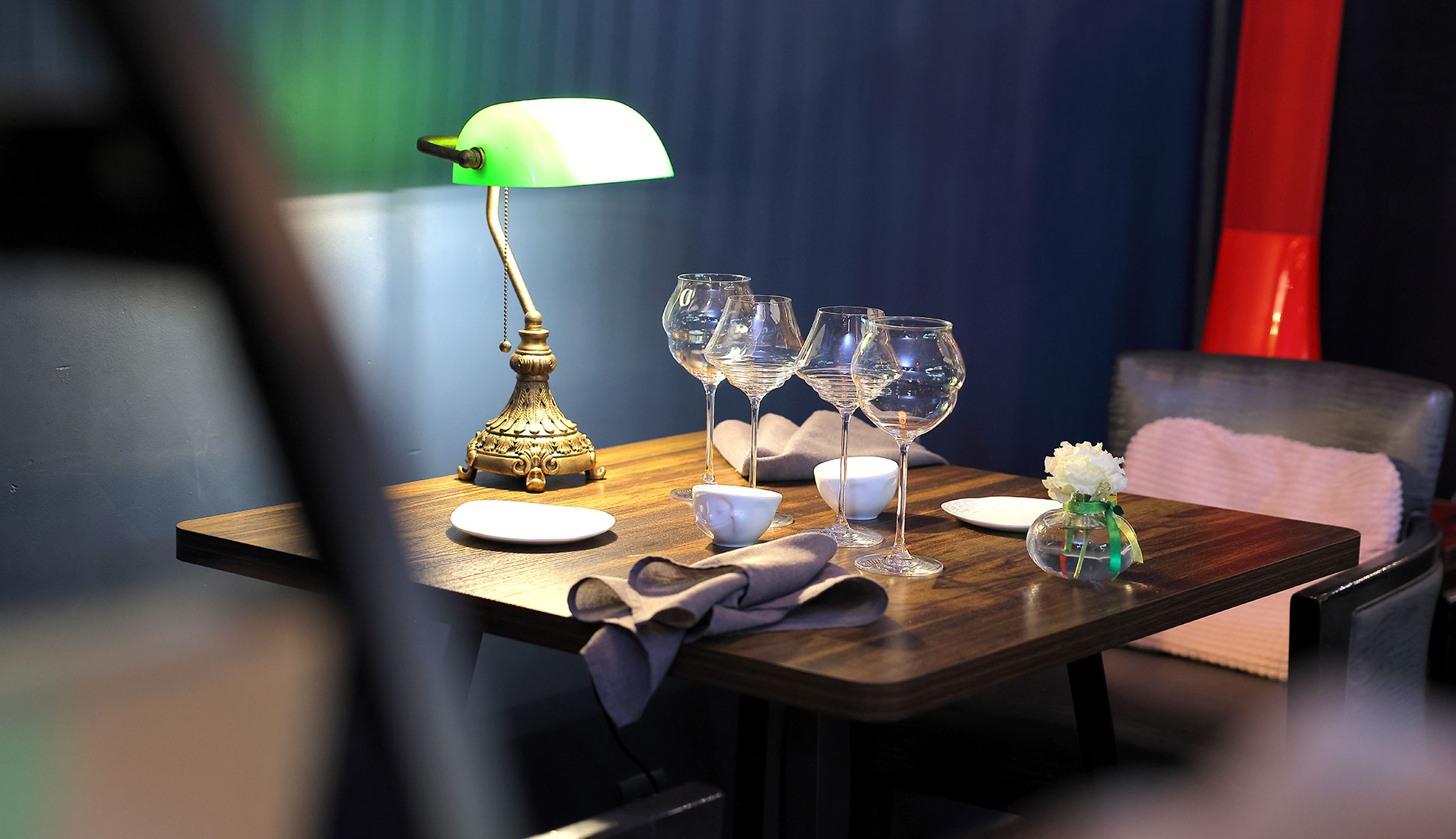 Table dressée en bois avec lampe de bureau à abat-jour vert, verres à vin et nappe grise au restaurant Croizard à Nîmes